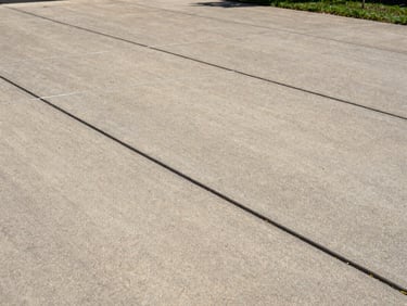 Close-up medium shot of a residential concrete driveway in Louisville, showing tight control joints and a broom-finish texture under natural daylight, sharp edge detail along the driveway border, no people