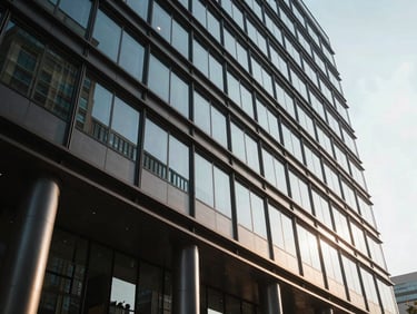 Low angle architectural perspective of a modern glass corporate headquarters, high-contrast natural light, sharp shadows.