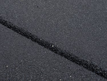 Close-up of fresh dark asphalt surface texture under overcast daylight, aggregate visible, smooth finished edge, documentary framing