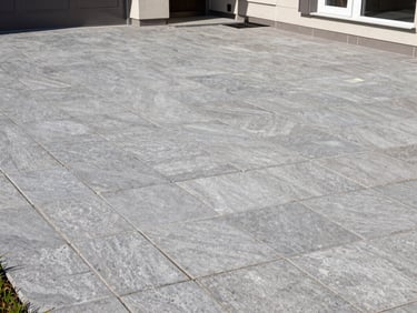 Wide shot of a completed interlocking stone patio beside a residential home, uniform grey pavers, crisp edge joints, natural daylight, no people