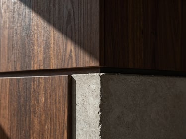 Extreme close-up of premium dark oak paneling meeting a poured concrete pillar, sharp architectural shadows, natural light.