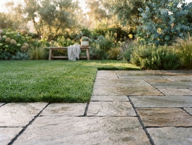 A beautifully finished stone patio with crisp joint lines meeting lush green turf under soft morning light, 35mm photography