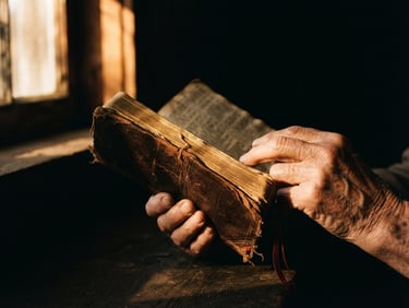 Dramatic documentary photography of hands holding a worn leather Bible under a single beam of warm amber window light, deep shadows, raw and emotional, 35mm lens