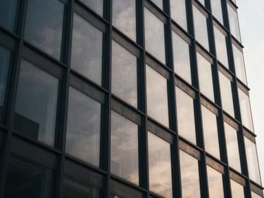 Abstract geometric pattern of overlapping glass panels on a skyscraper, reflecting soft natural daylight, muted navy and gold hues, shallow depth of field.