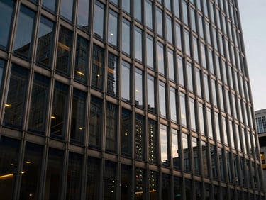 Wide architectural shot of a modern financial building facade at dusk, glass and steel reflecting city lights, deep navy and champagne tones, low contrast.