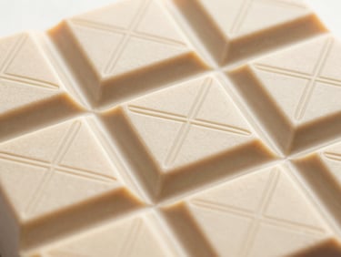 Premium chocolate bar packaging with complex geometric blind debossing on warm cream textured paper, elegant gold foil details, soft side light