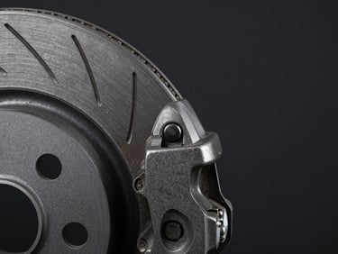 Macro close-up of a ventilated brake disc rotor edge and caliper bracket on a dark matte background, dramatic side-lighting emphasizing cast iron texture and venting slots