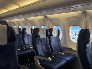 Intérieur moderne d'un avion avec des sièges confortables et un hublot montrant un ciel bleu, éclairé par une lumière douce et chaude.