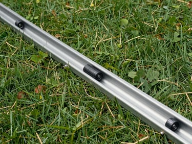 Eye-level shot of a clean garage door track, showing the rollers inside, with a slight bend being corrected by a tool, bright daylight.
