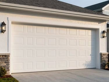 New white residential garage door installed flush on a suburban home exterior, late-afternoon daylight, clean driveway, no staging