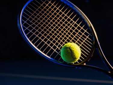 Close-up of a tennis racket hitting a yellow ball on a dark court, royal blue neon glow, golden specular highlights, 35mm