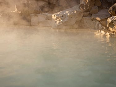Wide shot of a serene, unpeopled subterranean thermal pool, soft golden light filtering from above, smooth stone walls, muted beige and alabaster tones. warm editorial photography, soft golden-hour light, muted beige and alabaster tones, shallow depth of field, 35mm film style.