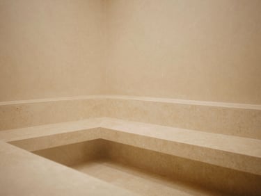 Interior of a minimalist steam chamber, smooth travertine benches, soft mist, subtle lighting, unpeopled, muted tones. warm editorial photography, soft golden-hour light, muted beige and alabaster tones, shallow depth of field, 35mm film style.