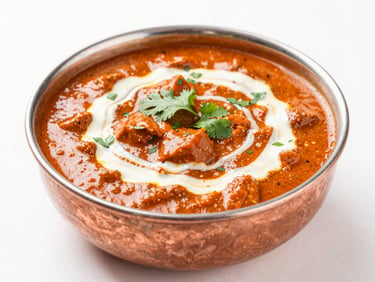 Bright high-key food photography, soft natural daylight, a copper bowl of rich red butter chicken curry, swirled cream, fresh coriander on top