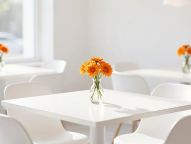 Bright, high-key shot of a modern, sunlit restaurant interior with minimalist white table settings and a small vase of warm orange flowers, soft daylight