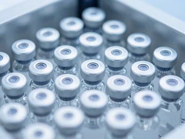 Close-up of pharmaceutical injection vials on an automated packaging line, sterile cool blue and white tones, bright high-key laboratory lighting, sharp macro focus, 35mm