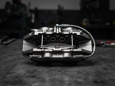 Crisp technical product photography of a pristine, unboxed metallic luxury car brake caliper on a dark industrial surface, high-contrast studio lighting, 50mm lens