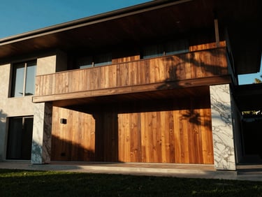 Sun-drenched luxury villa facade with teak wood panels and marble pillars, dramatic low-angle sunlight casting long shadows, 35mm.