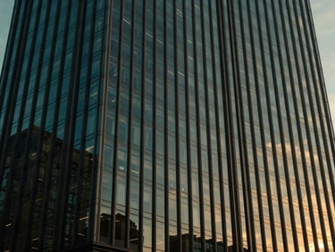Cinematic architectural photography of a modern glass skyscraper facade at twilight, deep navy and emerald tones, golden hour light reflecting off windows
