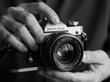 Extreme close-up of hands adjusting a vintage 35mm film camera lens, moody indoor shadows, high contrast black and white