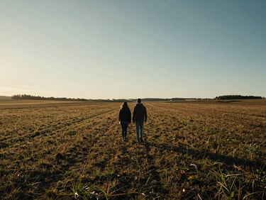 Wide cinematic landscape of a couple walking away in an open field at golden hour, deep shadows, high contrast.