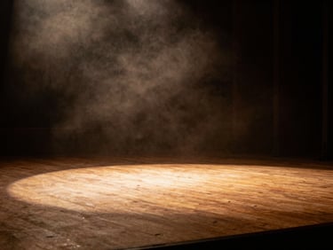 Wide cinematic low-light shot of a single warm stage light casting long shadows across an empty wooden stage, amber glow, atmospheric smoke, negative space on the left.