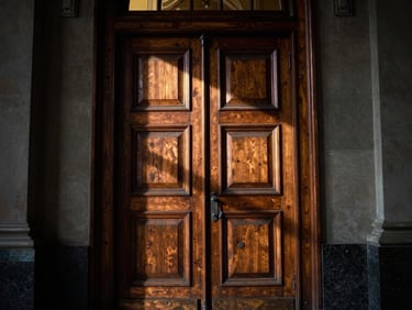 Detail shot of a heavy, ornate wooden door of a classic institutional court building, slightly ajar, with deep shadows emphasizing its imposing presence, 35mm.