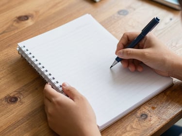 Close-up of hands holding a school savings notebook, warm natural light, rustic wooden table background.