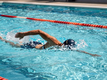 Entraînement physique intense dans la piscine d'Angoulême, vagues de surface créées par un nageur en plein effort de sauvetage, lumière du jour vive.
