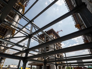 Wide-angle architectural shot of a massive steel-framed G7 construction site in Kuala Lumpur, sharp daylight, structural steel beams framing the sky, high-contrast industrial composition.