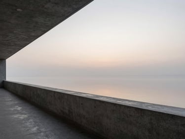 A wide, calm environmental shot of a quiet architectural concrete balcony overlooking a soft, misty horizon at dawn, generous negative space on the right.