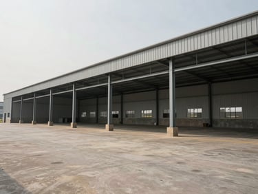Wide shot of a completed industrial warehouse facility with steel structure and concrete apron, exterior view under flat overcast daylight, no workers or people, muted palette of grey and beige