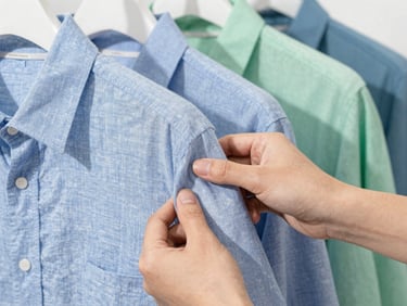 Close-up of high-quality fabric textures, hands touching a linen shirt on a hanger, bright natural daylight, clean professional photography