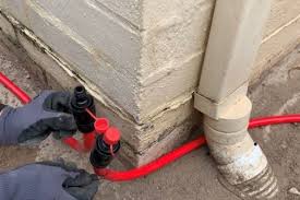 A technician installs a termite chemical barrier system with red piping along a home foundation.
