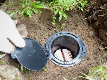 A person installs a termite bait station in the ground to protect a home from pest infestation.