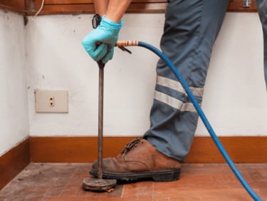 Professional pest control technician using a soil injector for termite treatment in a home.