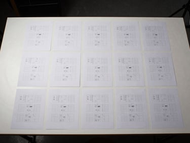 Bird's-eye view of a studio workstation, a grid of printed layout sheets arranged in precise rows on a matte white surface under studio strobe lighting, no hands or people visible