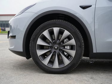 Close-up side profile of a zero-emission vehicle front wheel and brake assembly on a neutral grey concrete lot, overcast daylight, sharp mechanical detail, no people