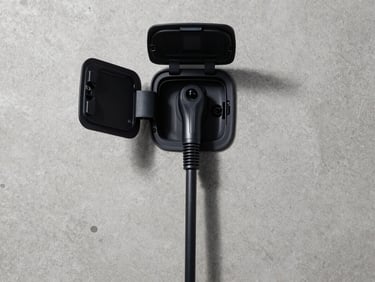 Overhead flat-lay of an electric vehicle charging port and cable on a clean concrete surface, studio strobe lighting, no humans, minimal composition