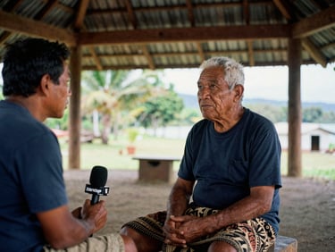 A local Samoan journalist interviewing an elder in a traditional open-sided fale, natural Pacific daylight, rich documentary tones, sharp focus.