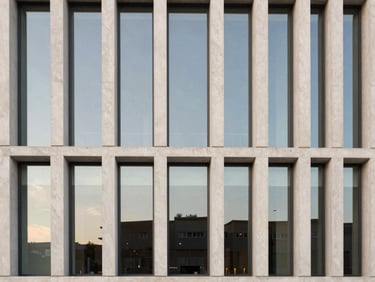 Geometric wide shot of a modern luxury building facade, architectural concrete, large glass windows reflecting a soft sky, clean vertical lines, medium format