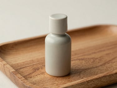 A ceramic essential oil bottle on a textured wooden tray, soft diffused daylight, muted sage tones