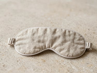 A folded linen eye mask resting on a textured stone surface, soft morning daylight, muted beige tones