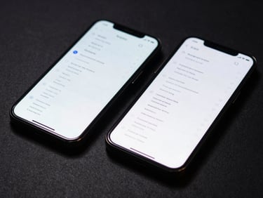 Close-up of two smartphones side by side on a matte dark surface displaying native app interfaces with structured data lists, cool studio strobe from above, sharp screen glare, no hands or people