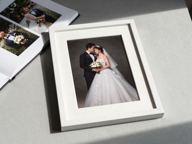 Flat lay of a framed wedding portrait print resting on a light grey surface next to a printed photo album, natural north-facing daylight, no people in frame, clean and precise styling