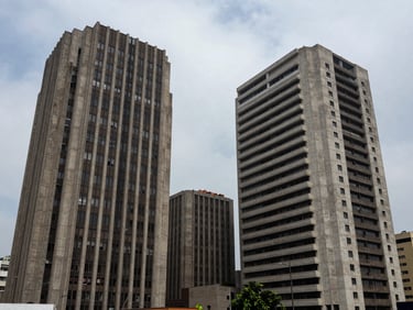 Extreme wide architectural shot of brutalist corporate buildings in San Isidro, Lima, under overcast coastal daylight. High-contrast shadows, sharp lines, generous negative space.
