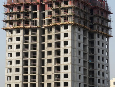 Wide documentary shot of a high-rise residential construction site at finishing stage, Mumbai, natural daylight, scaffolding partially removed revealing completed lower floors with window glazing installed, structural concrete and facade cladding panels visible side by side, no workers posed, factual site record framing