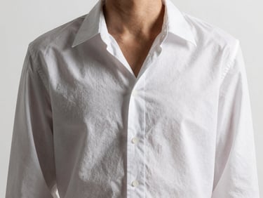 High-fashion studio model shot showing the clean drape of a minimalist white cotton blouse, high-contrast lighting