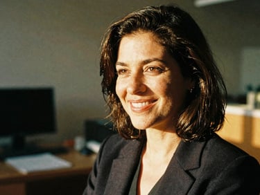 Candid portrait of a smiling woman in her 40s in a warm, sunlit office setting, looking off-camera, 35mm film look