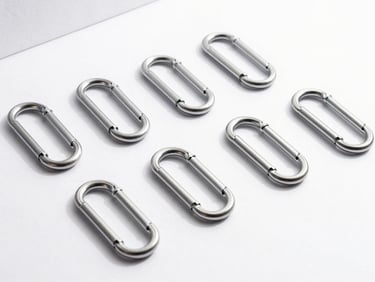 Sleek brushed steel carabiners and hooks arranged neatly on a clean white surface with soft shadows.